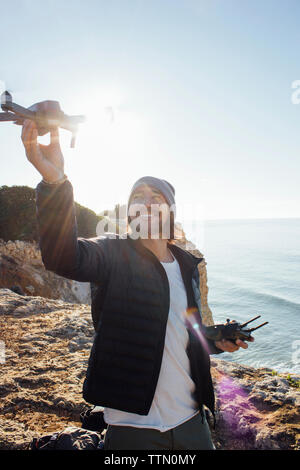 Lächelnd Mann fliegen Quadcopter, während am Strand gegen den klaren Himmel stehen während der sonnigen Tag Stockfoto