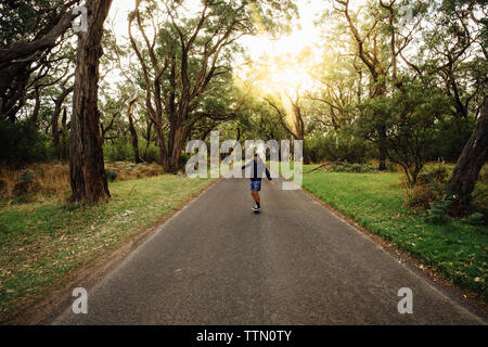 Mann skateboarding auf der Straße inmitten von Bäumen im Wald gegen Himmel bei Sonnenuntergang Stockfoto