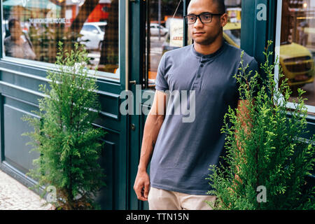 Nachdenklichen jungen Mann weg schauen beim Stehen gegen Coffee Shop in der Stadt Stockfoto