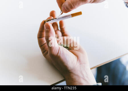 7/8 der Menschen Hand holding Marihuana Gelenke während Zigarette Reißen am Tisch Stockfoto