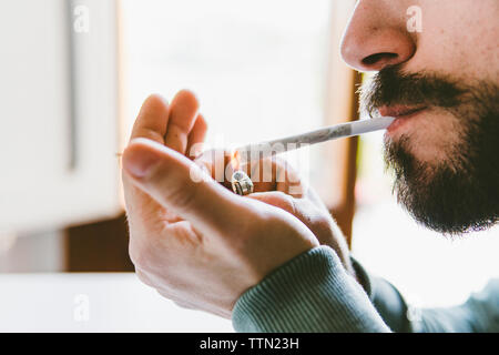 Mittelteil des bärtigen Mannes entzünden Marihuana gemeinsame mit Zigarettenanzünder zu Hause Stockfoto