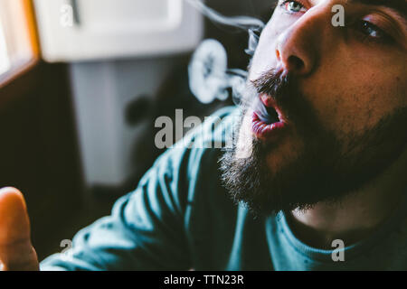 Nahaufnahme des bärtigen Mannes ausatmen Rauch, während das Rauchen von Marihuana joint zu Hause Stockfoto