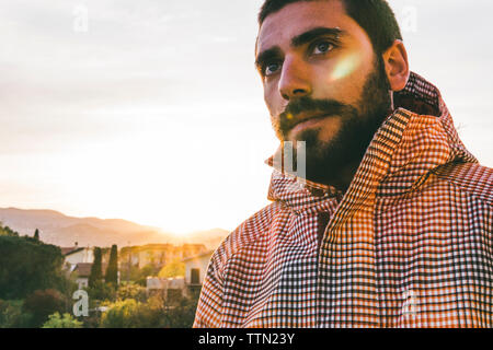 Nachdenklichen jungen Mann mit T-Shirt unterwegs gegen Himmel bei Sonnenuntergang Stockfoto