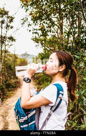 Seitenansicht der weiblichen Wanderer Trinkwasser im Stehen von Pflanzen gegen Sky Stockfoto