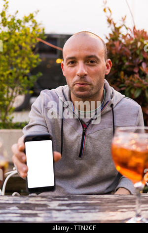 Portrait der balding jungen Mann zeigt leere Smart Phone bei Tisch sitzen Stockfoto