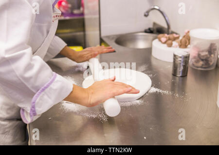 Mittelteil der weiblichen Baker rollt Teig auf den Küchentisch im Labor Stockfoto