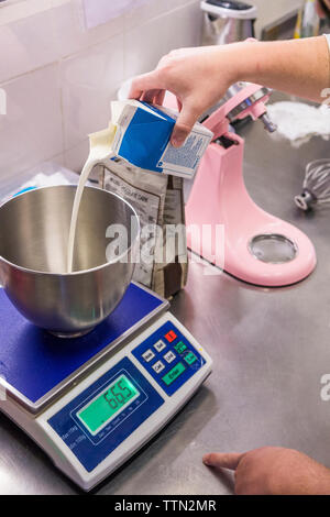 7/8 Händen der männlichen Bäcker gießen Milch in Schüssel auf der Waage im Labor Stockfoto