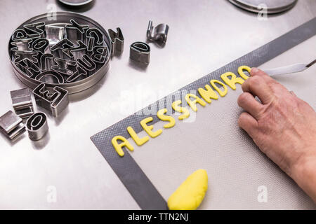 7/8 Hand von Frau Baker, die die Alphabete mit Teig auf Blatt in der Küche Stockfoto