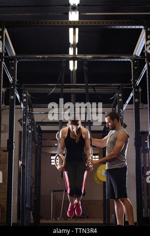 Männliche Athleten Unterstützung der Frau in Ausübung auf Gymnastik Ringe im Fitnessstudio Stockfoto