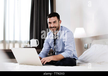Portrait von Happy Geschäftsmann sitzt mit Laptop auf dem Bett im Hotelzimmer Stockfoto