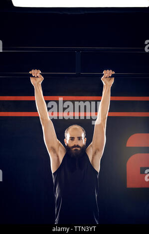 Portrait von zuversichtlich männlichen Athleten hängen von Monkey Bar in der Turnhalle Stockfoto