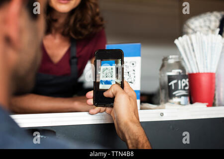 Zugeschnittenes Bild des Kunden die Zahlung durch Smart Phone in Essen Lkw Stockfoto