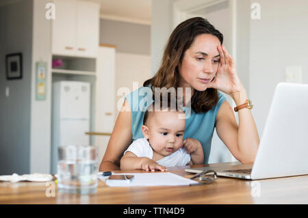 Frustrierte Mutter mit Baby Boy mit Laptop Computer zu Hause. Stockfoto