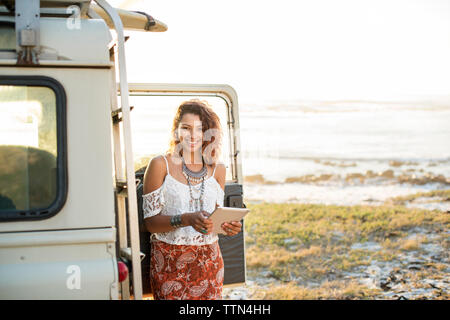 Portrait von Frau mit Tablet-PC von Geländewagen am Strand Stockfoto