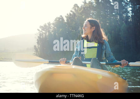 Lächelnde Frau Kajakfahren auf dem See gegen Himmel während der sonnigen Tag Stockfoto