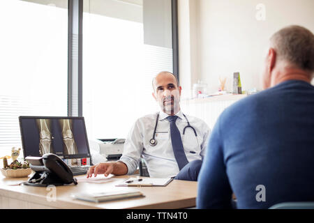 Arzt im Gespräch mit dem Patienten beim Sitzen am Schreibtisch im Krankenhaus Stockfoto