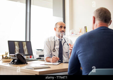Arzt diskutieren mit Patient beim Sitzen am Schreibtisch im Krankenhaus Stockfoto
