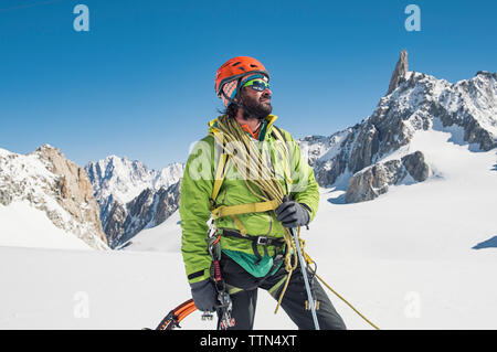 Wanderer mit Kletterausrüstung stehend auf schneebedeckten Berg gegen den klaren blauen Himmel Stockfoto