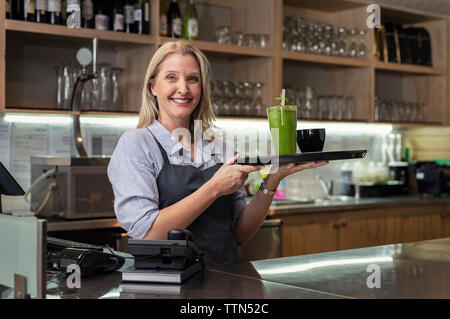 Portrait von lächelnd weibliche Eigentümer holding Willkommenstablett mit Getränken, während in der Cafeteria stehen Stockfoto