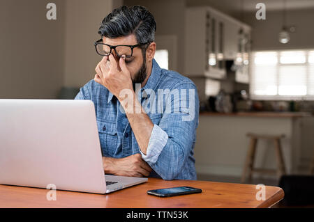 Betonte Geschäftsmann mit Laptop auf hölzernen Tisch zu Hause sitzen Stockfoto