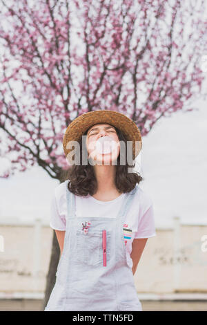 Junge Frau blasen Bubble Gum, während gegen cherry tree in PARK-Stellung Stockfoto