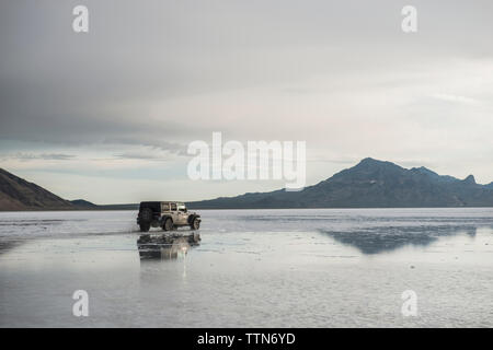 Sport Utility Vehicle in Bonneville Salt Flats gegen Berge und Himmel Stockfoto