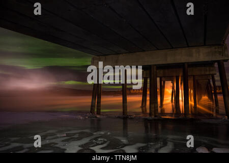 Low Angle View von Aurora Borealis über Meer mit hölzernen Pier im Vordergrund Stockfoto