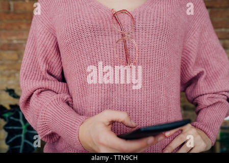 Mittelteil der Frau tragen Pullover bei der Verwendung von Smart Phone Stockfoto