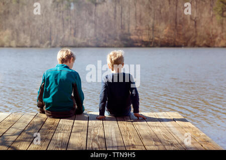 Ansicht der Rückseite des Jungen sitzen auf Pier über den See Stockfoto