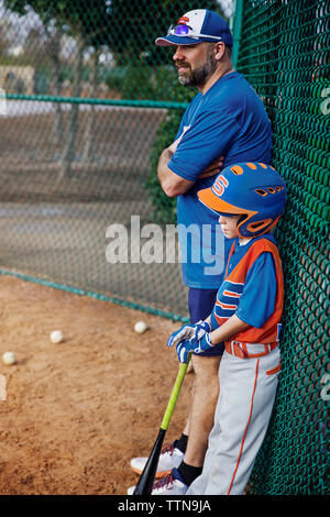 Seitenansicht von nachdenklich Baseball Spieler und Trainer stehen chainlink Fence auf Feld Stockfoto