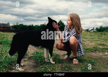 Jugendmädchen Streichelzoo Hund während kauert auf dem Feld gegen die stürmischen Wolken Stockfoto