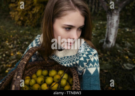 Nahaufnahme der nachdenkliche Frau mit Weidenkorb mit Zitronen während der Sitzung in Hof Stockfoto