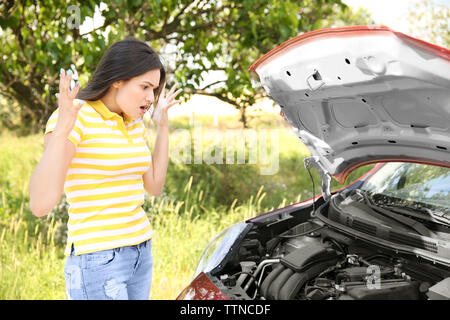 Junge Frau, die in der Nähe von Broken Auto Stockfoto