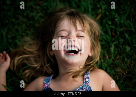5-Jähriges Mädchen lachen mit blauen Lippen aus Lollipop, liegend im Gras Stockfoto
