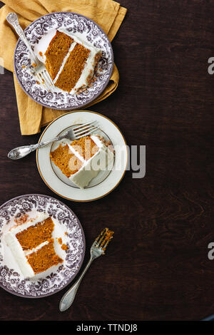 Blick aus dem hohen Winkel auf die Kuchenscheiben, die in Tellern mit Gabeln auf dem Holztisch zu Hause serviert werden Stockfoto