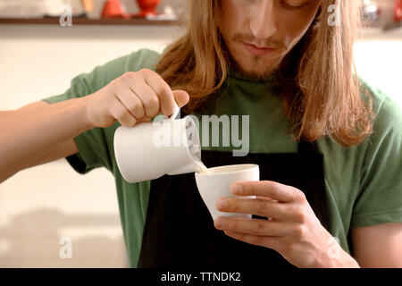 Man gießt Sahne im Kaffee Stockfoto