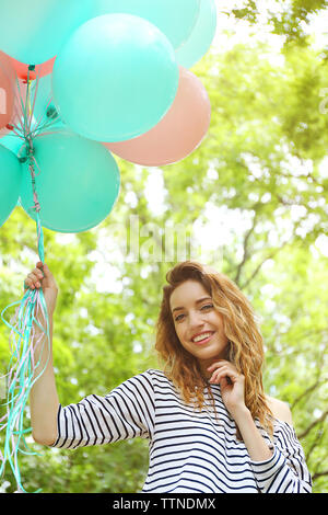 Schöne junge Frau mit bunten Luftballons in Park Stockfoto