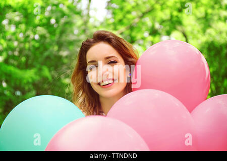 Schöne junge Frau mit bunten Luftballons in Park Stockfoto