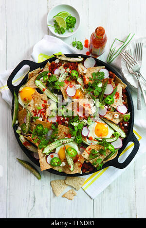 Hochwinkelansicht von Nachos mit Gemüse und Spiegeleiern in Kochtopf auf Holztisch zu Hause Stockfoto