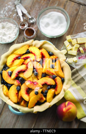 Hochwinkelansicht von Pfirsichen und Heidelbeeren in Kuchenteig auf dem Tisch zu Hause Stockfoto