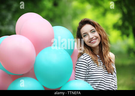 Schöne junge Frau mit bunten Luftballons in Park Stockfoto