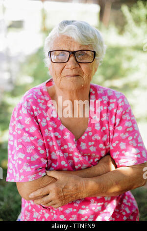 Portrait der älteren Frau mit gekreuzten Armen Tragen von Brillen im Hinterhof Stockfoto