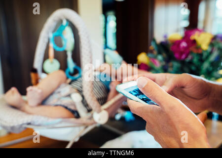 Zugeschnittenes Bild von Hand und mit Hilfe smart phone von Baby in den Sitz zu Hause Stockfoto
