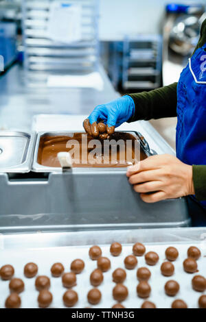 Mittelteil der Köchin Eintauchen in Stücke Schokolade Fondue im Werk Stockfoto