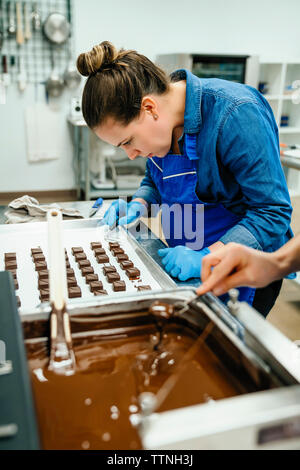 7/8 Hand des Chefkochs Eintauchen in Schokoladen Fondue, die während der Arbeit mit Kollegen im Werk Stockfoto