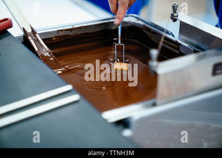 7/8 Hand der Köchin eintauchen Schokolade mit Gabel im Fondue im Werk Stockfoto