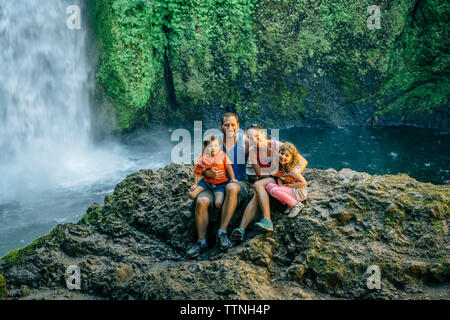 Portrait von Happy Family sitzen auf den Felsen gegen Wasserfall im Wald Stockfoto