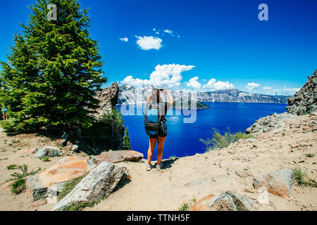 Ansicht der Rückseite des weiblichen Wanderer mit Rucksack fotografieren, während sich gegen Crater Lake Stockfoto