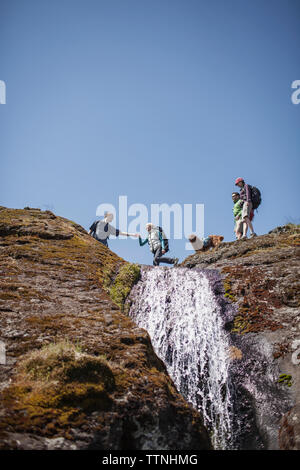 Low Angle View von Freunden Wandern auf den Berg gegen den klaren Himmel Stockfoto