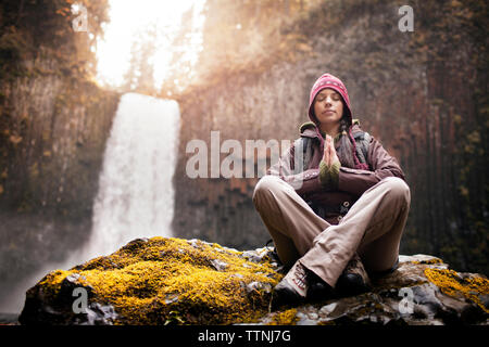 Frau meditieren auf Rock mit Wasserfall im Hintergrund Stockfoto